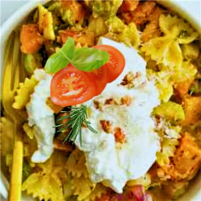 A bowl of cooked multicoloured Farfalle Pasta in a bowl garnished with sourcream and sliced tomatoes.