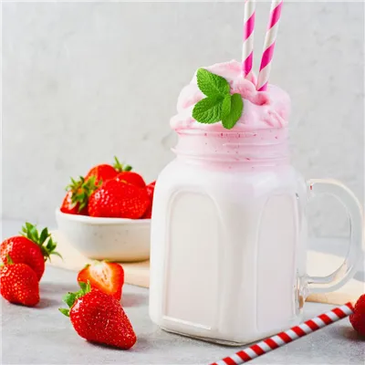 Milk topped with strawberry pink cream garnished with mint leaf, on a table scattered with fresh strawberries.