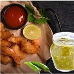 Platter of fried nibbles with cut lemon, a black bowl of tomato ketchup and a jar of green chillie sauce.