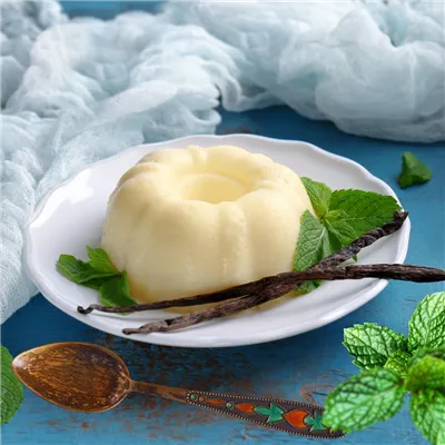 White Vanilla Pudding  on a white plate, garnished with vanilla pods and mint leaves.