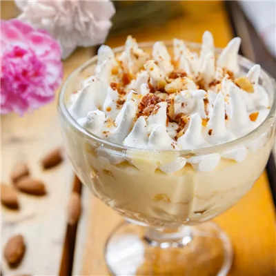 Almond Pudding in a glass dessert cup, topped with cream and crushed almonds, on a wooden table.