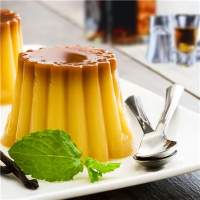 Bourbon Vanilla Pudding  on a white plate garnished with mint and dessert cutlery on side of plate.