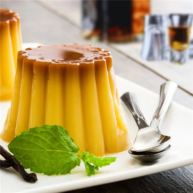 Bourbon Vanilla Pudding  on a white plate garnished with mint and dessert cutlery on side of plate.