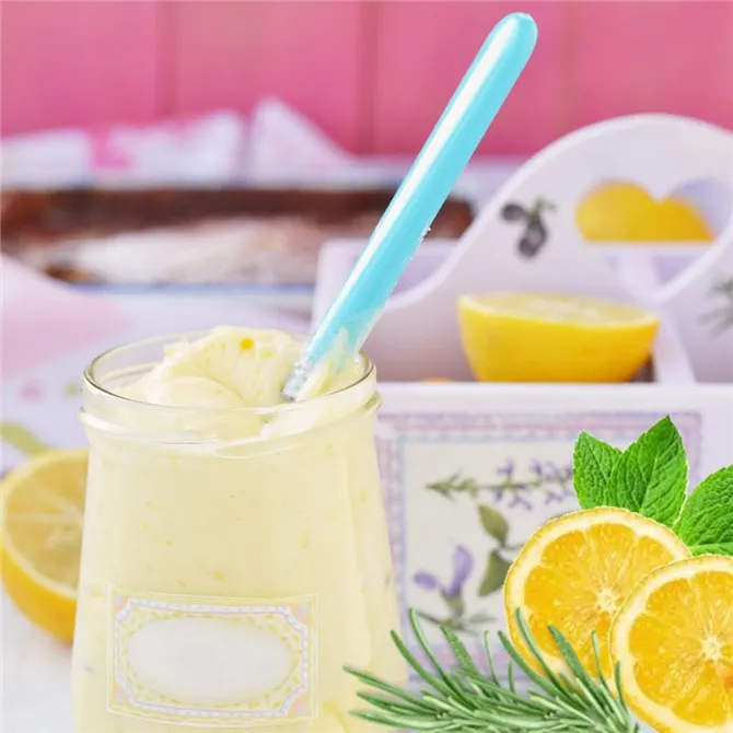A glass of yoghurt puddinglike dessert on a table with lemons and herbs on it.