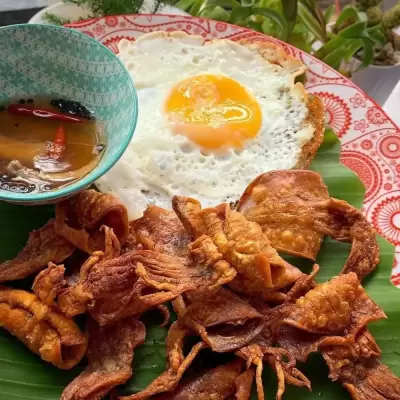 Fried cuttlefish squids on a plate with fried bullseyes egg and a small bowl of vinegar dip.