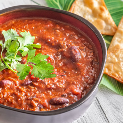 Bowl of Chilli Concarne in a grey bowl garnished with cilantro, on an ash grey wooden table.