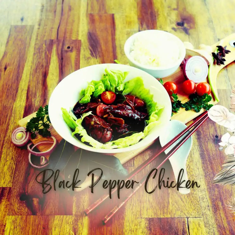Black pepper chicken in a bowl lined with lettuce, with chopsticks and fresh garnishes on a wooden board