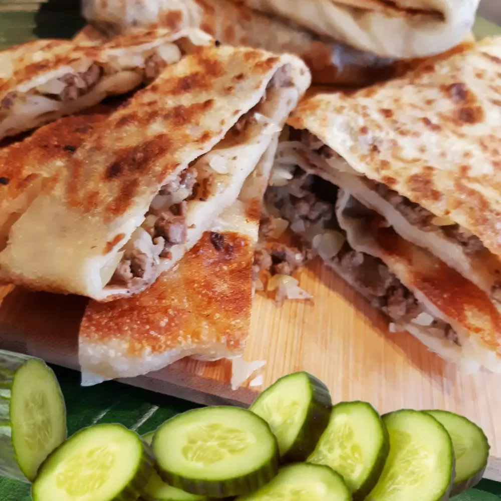 Golden pan-fried murtabak, a roti filled with mince, cut open beside cucumber slices