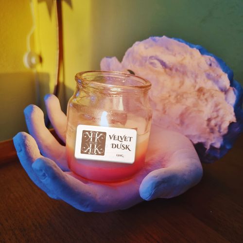 A blue cast hand holding a lit candle jar