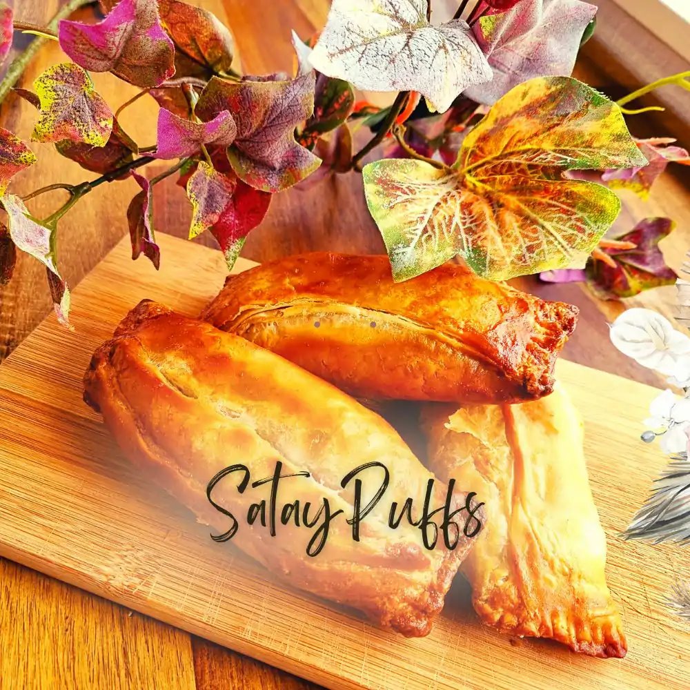 Golden baked satay puff pastries on a wooden board with decorative flowers and leaves
