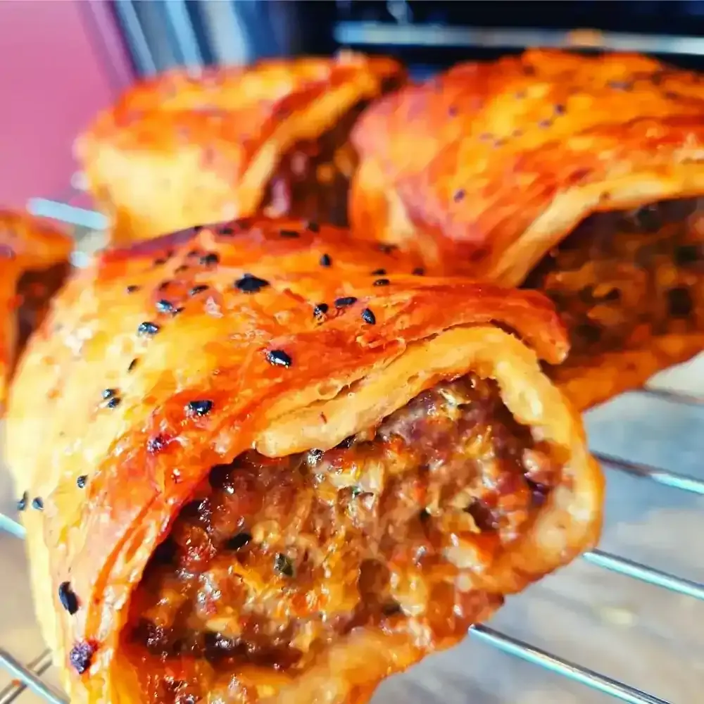 Golden flaky sausage rolls with sesame seeds cooling on a rack